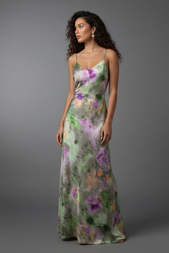 A woman wearing a floral tie-dye maxi dress with a removable scarf, standing near a pink wall.